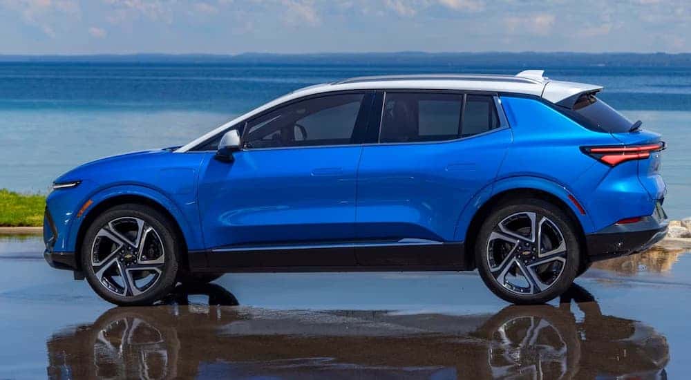 Side angle view of a blue 2025 Chevy Equinox EV parked on wet pavement.