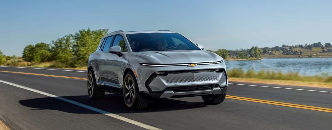 A silver 2025 Chevy Equinox EV is shown driving past a lake.