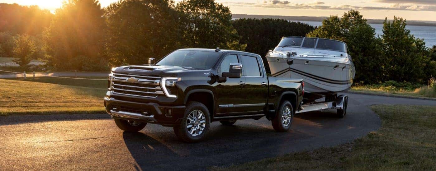 A black 2024 Chevy Silverado 2500 HD is shown towing a boat after visiting a Chevy Silverado dealer.