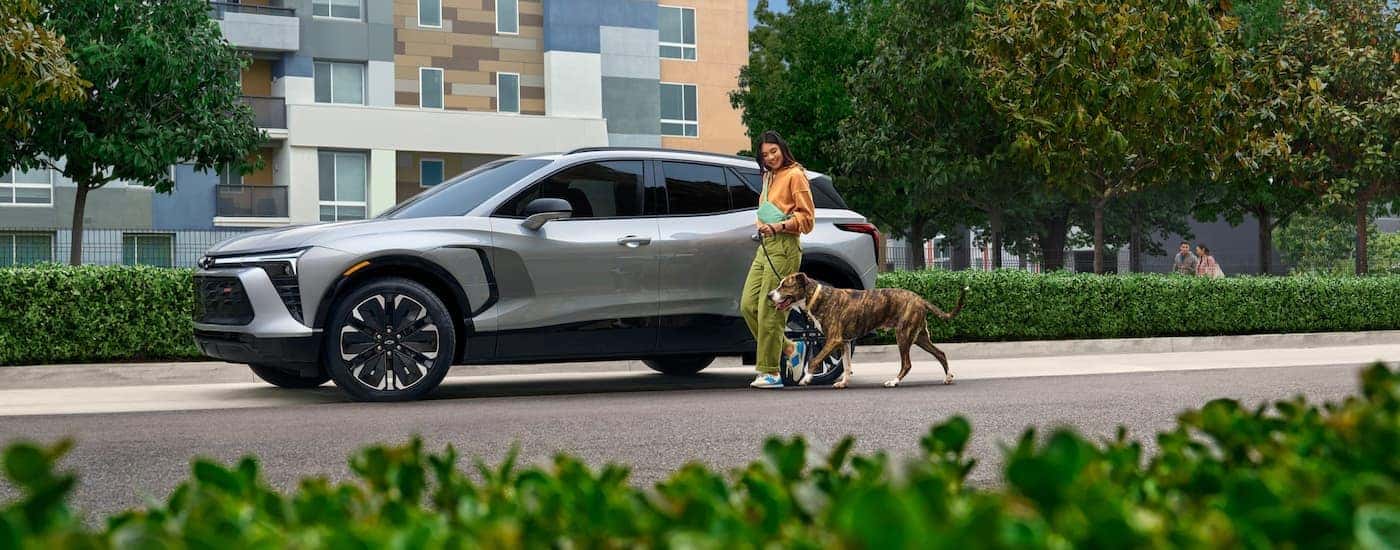 A person is shown walking a dog near a grey 2024 Chevy Blazer EV RS.