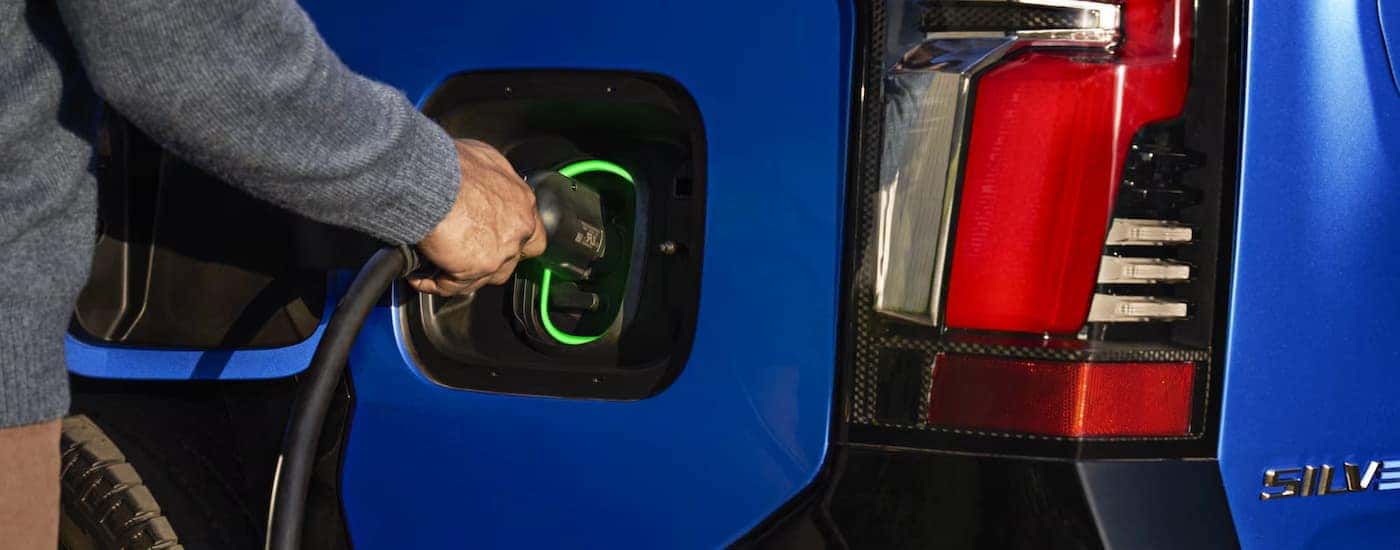 A man plugging in a blue 2025 Chevy Silverado EV