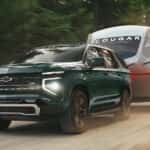 Green 2026 Chevy Tahoe Z71 towing a camper down a dirt road.