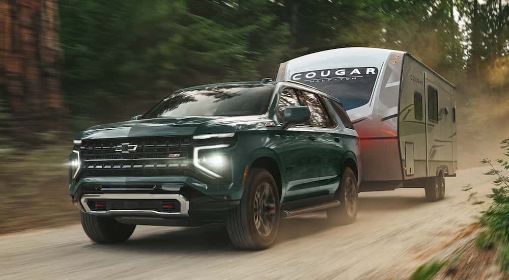 Green 2026 Chevy Tahoe Z71 towing a camper down a dirt road.