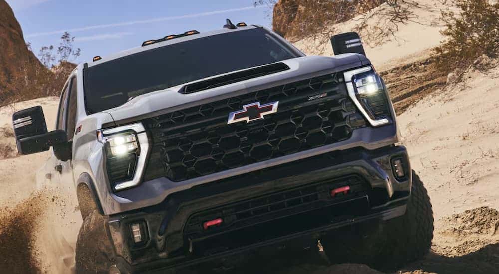 Front grille on a gray 2026 Chevy Silverado 2500 HD off-roading in sand