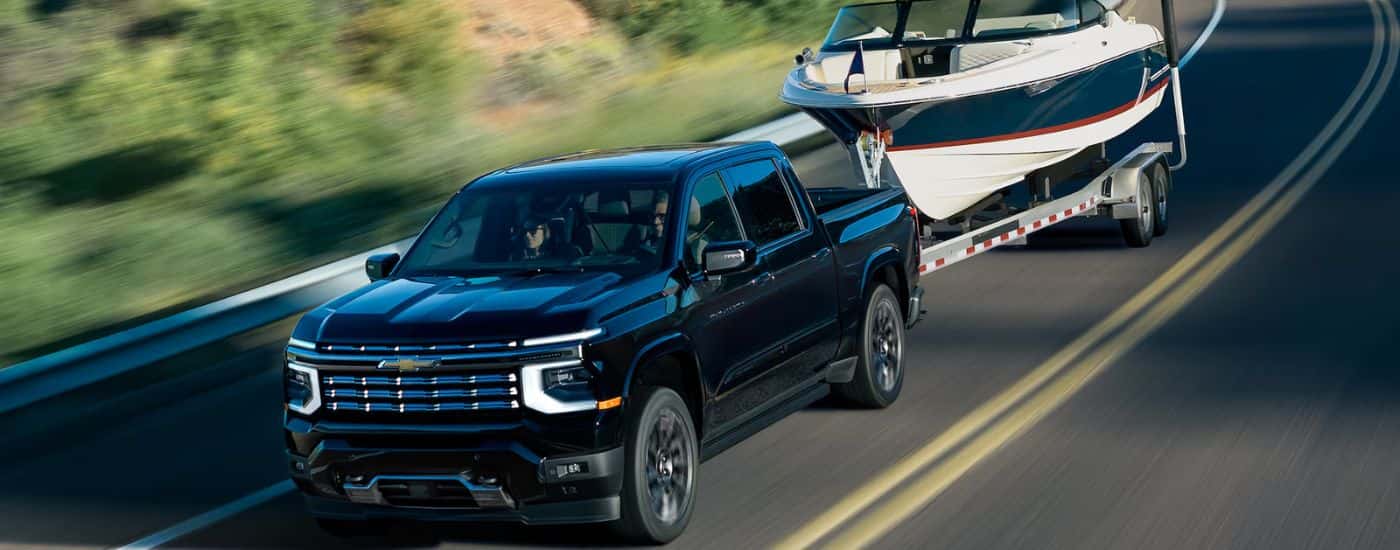 Black 2027 Chevy Silverado 1500 High Country towing a boat on a paved road.