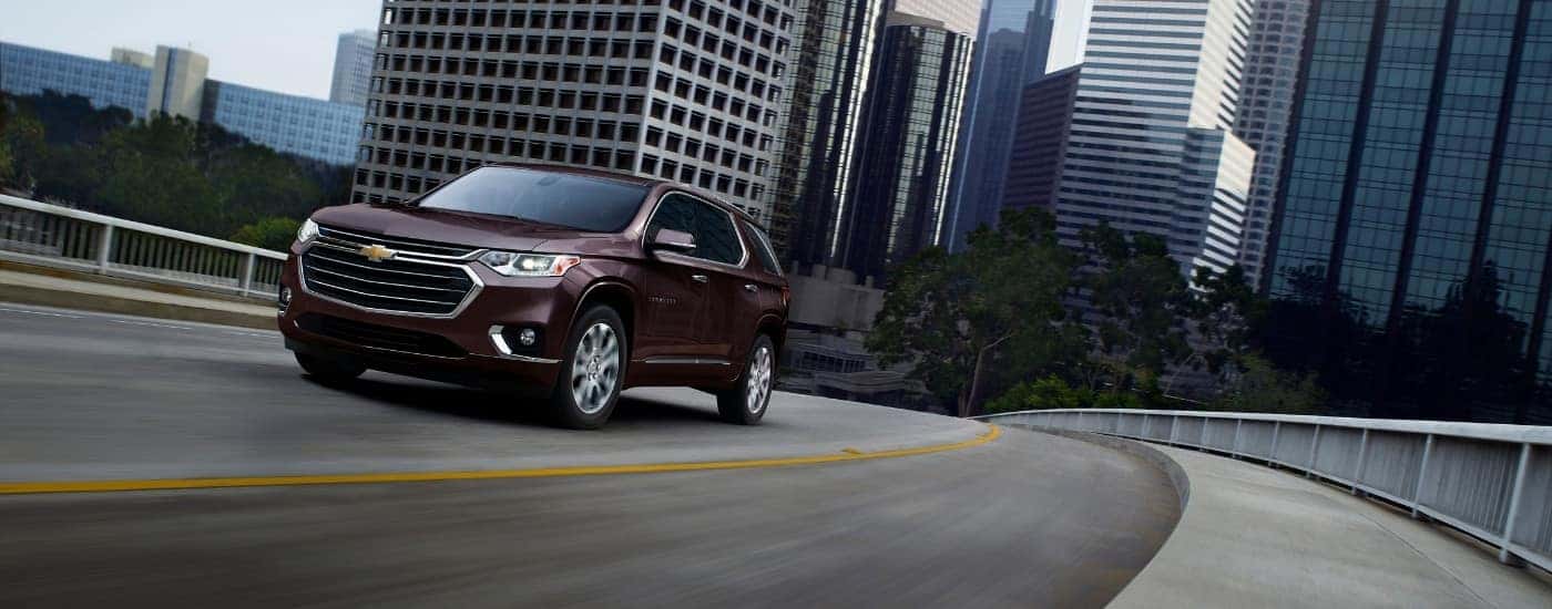 A maroon 2019 Chevy Traverse driving away from a city.