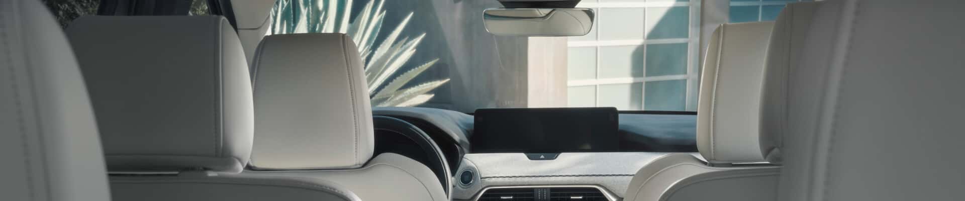 Interior view looking forward in a white leather Mazda CX-90 SUV facing a modern house.
