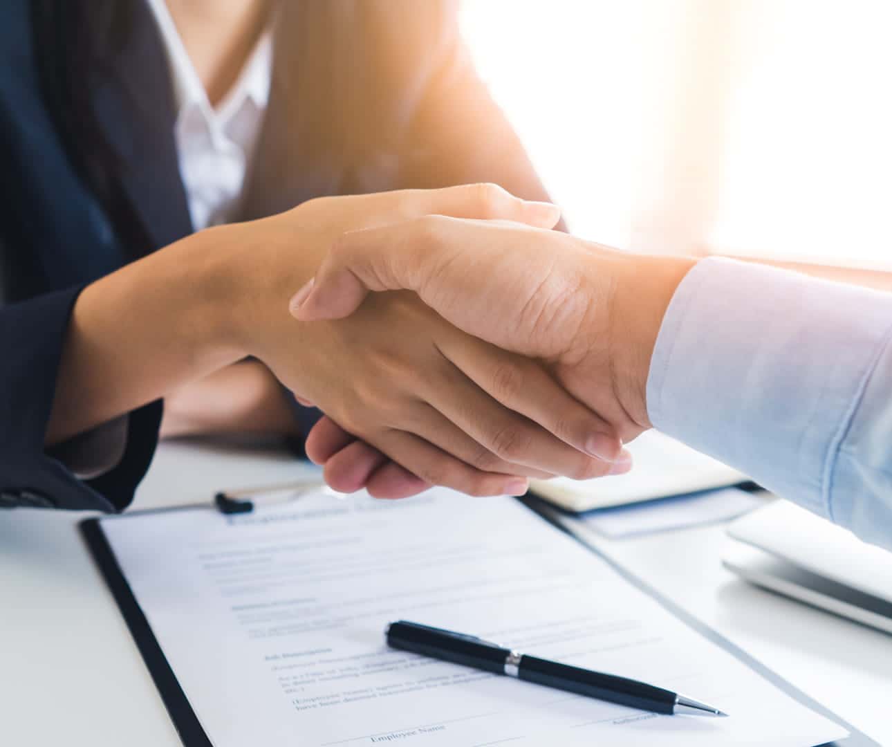 Two people shaking hands over paperwork on a desk.