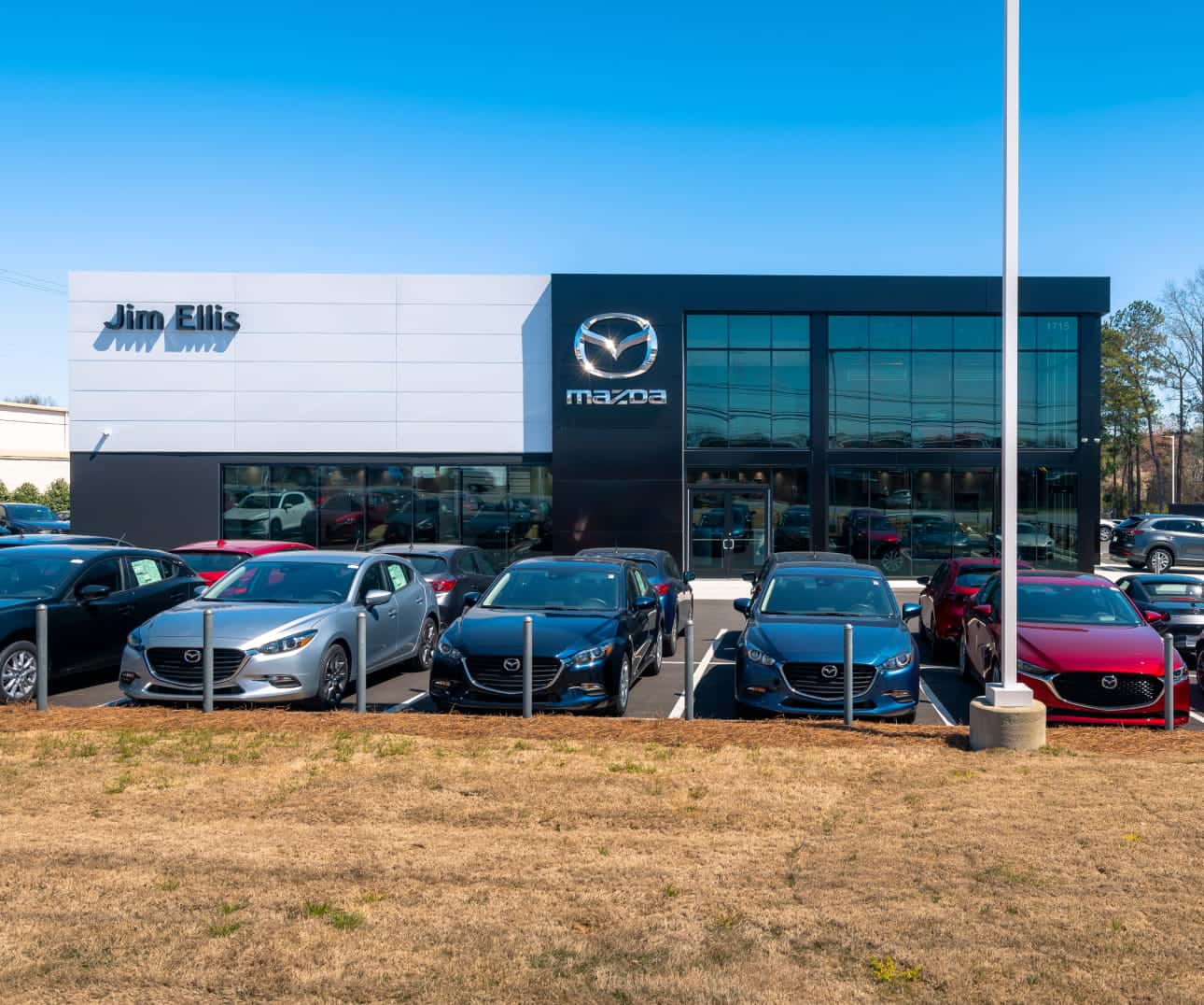 Exterior view of a Mazda dealership building with several vehicles parked in front under a clear blue sky.