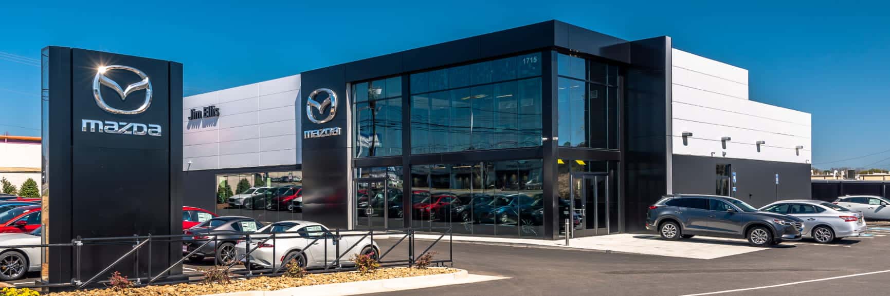 Exterior view of the Jim Ellis Mazda dealership featuring a modern glass-front showroom, Mazda signage, and several vehicles parked outside.