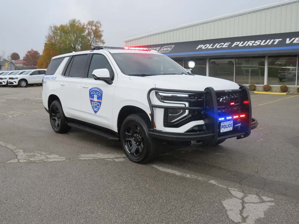 Front three-quarter view of a white 2025 Chevy Tahoe patrol vehicle with push bumper and LED warning lights.