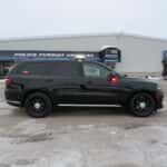Side profile of a 2025 Dodge Durango police unit featuring department decals, reflective striping, and rear flashers.