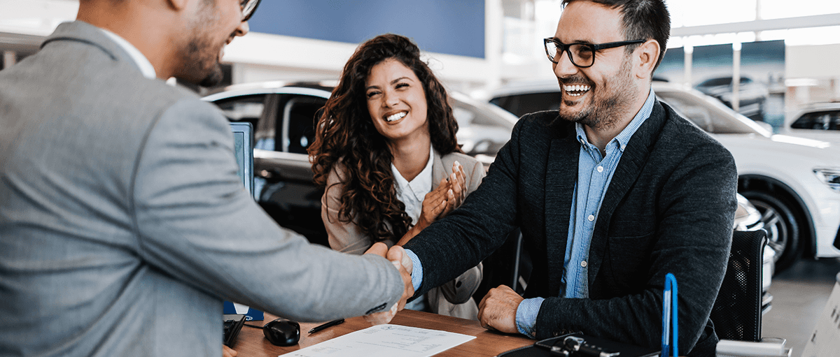 A man shakes a salesman's hand at a car dealership