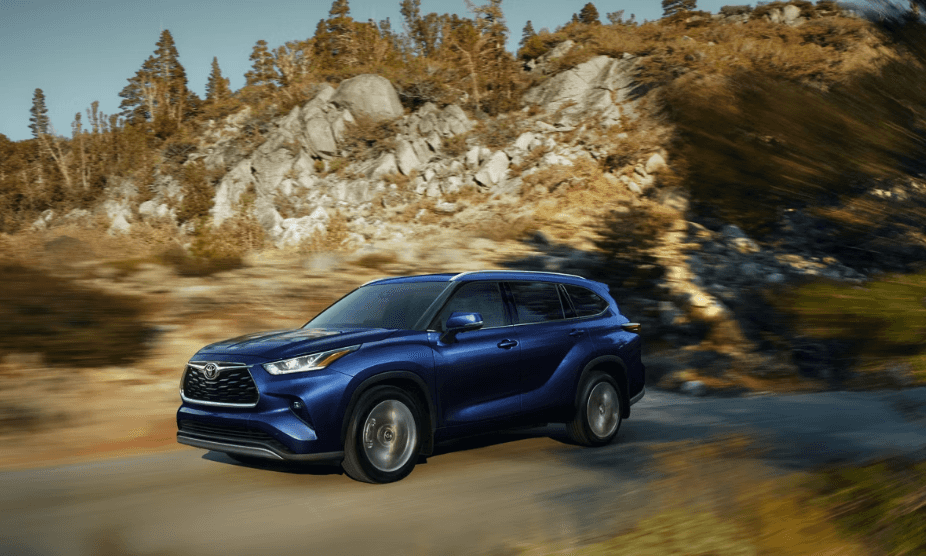 The 2026 Toyota Highlander is shown driving on a road through the mountains.