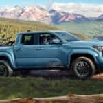 A light blue Toyota Tacoma with bikes in the truck bed driving up a mountain