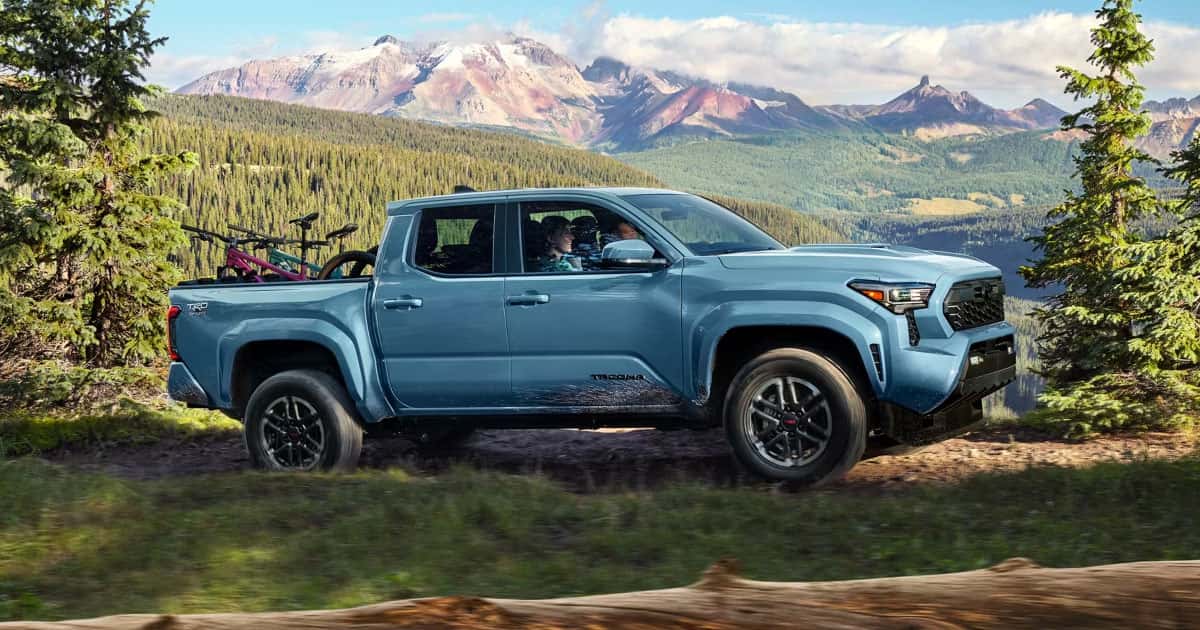 A light blue Toyota Tacoma with bikes in the truck bed driving up a mountain