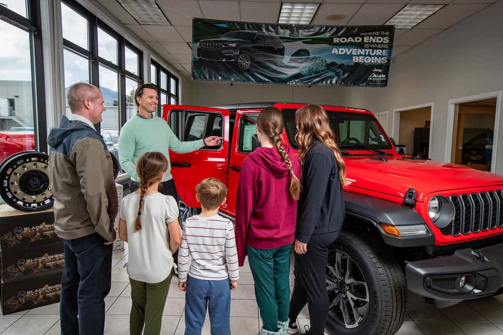 Juneau Jeep Ram team helping a local family shop for a red Jeep Wrangler inside the showroom
