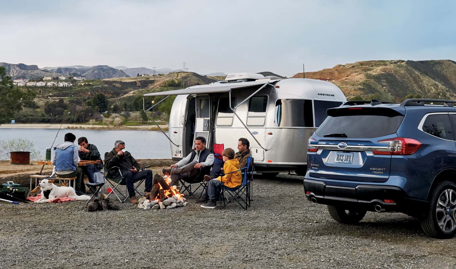 Family campfire scene near a lake with a Subaru