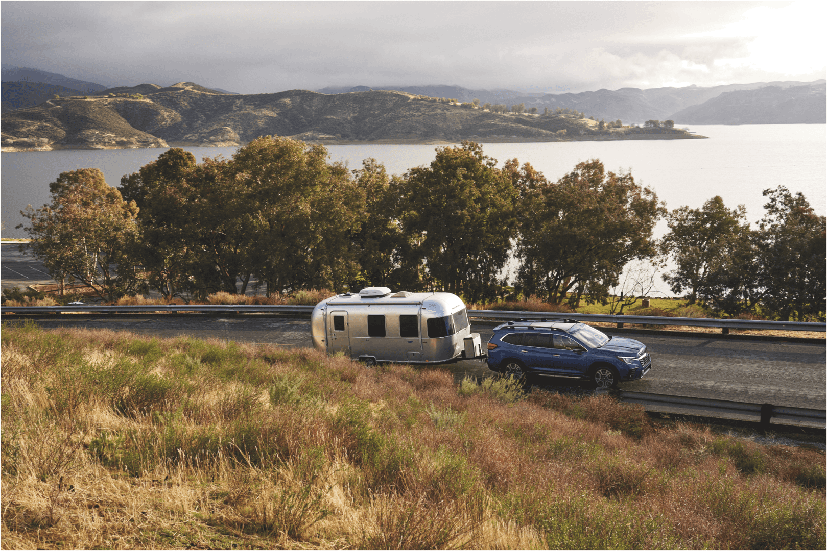 Subaru Outback towing a camper by a mountain lake