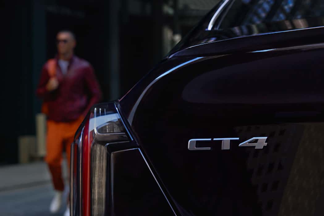 Cadillac 2026 CT4 Sport in Black Raven; CT4 Badge; male talent in orange; rear of vehicle