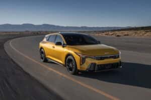2026 Kia K4 Hatchback in Sparkling Yellow driving on a desert highway, showcasing its aggressive front grille, LED lighting signature, and sporty aerodynamic design.
