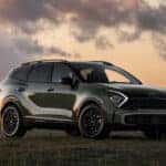 A green 2025 Kia Sportage parked in an open field at sunset, showcasing its rugged design and sleek headlights. Find your new Kia Sportage at Kia of Anderson.