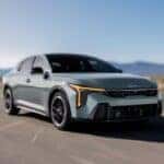 2025 blue gray kia k4 driving on through a desert road on a sunny day