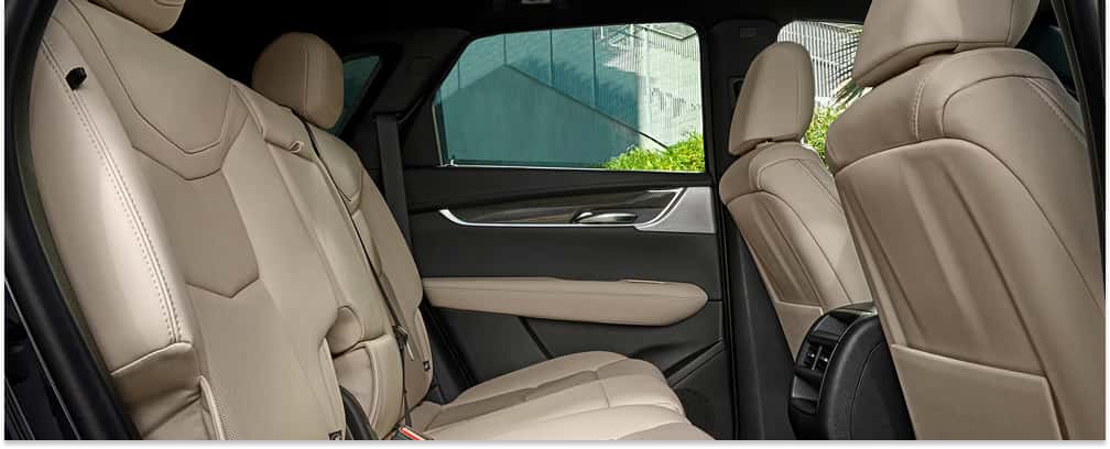 An interior view looking across the rear seats of a 2026 Cadillac XT5 featuring beige leather upholstery, dark door panels, and rear center console vents.