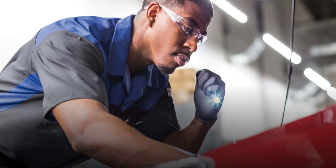 Service Tech looking under the hood of red vehicle in a service center.