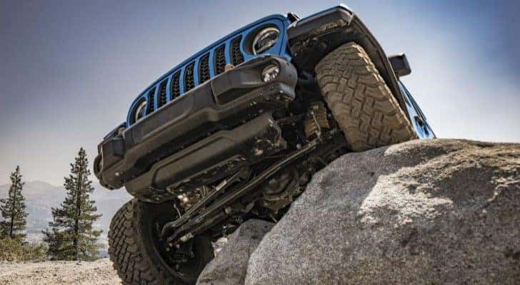 A blue 2022 Jeep Wrangler is shown crawling over rocks after leaving a Jeep dealer.