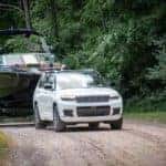 A white 2024 Jeep Grand Cherokee is shown towing a boat after leaving a Jeep dealer.