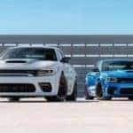 A white and a blue 2023 Dodge Charger SRT Hellcat are shown in front of bleachers.