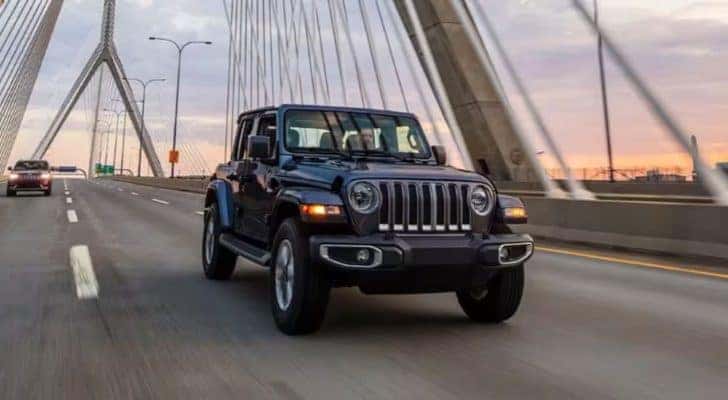 A black 2023 Jeep Wrangler is shown driving on a bridge.