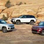 A silver 2024 Jeep Grand Cherokee, a white 4xe Trailhawk, and a maroon Grand Cherokee L are shown off-road.