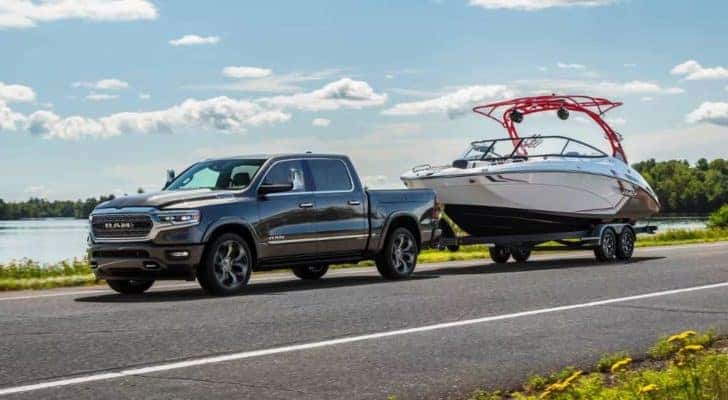 A grey 2024 Ram 1500 for sale is shown from the side while towing a boat.