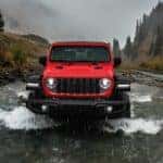 A red 2024 Jeep Wrangle for sale is shown driving through a river.