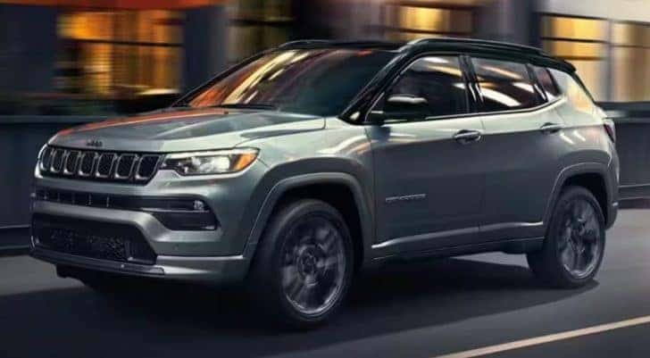 A grey 2023 Jeep Compass for sale driving through a city.