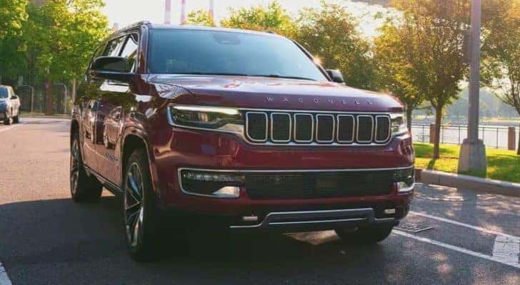 A maroon 2023 Jeep Wagoneer for sale is shown driving past trees.