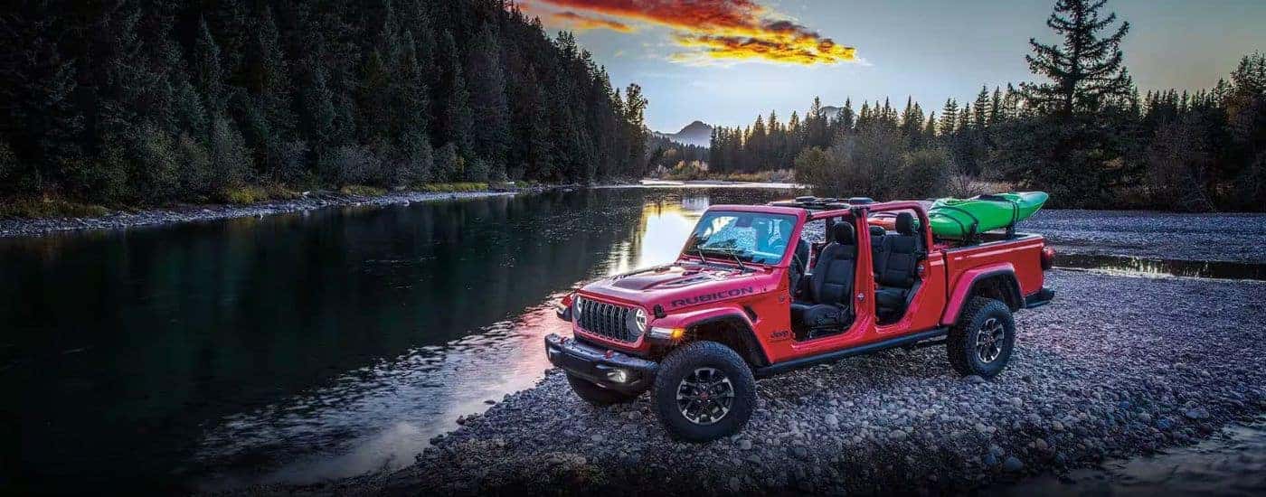 A red 2024 Jeep Gladiator Rubicon parked by a river with a kayak in the bed.
