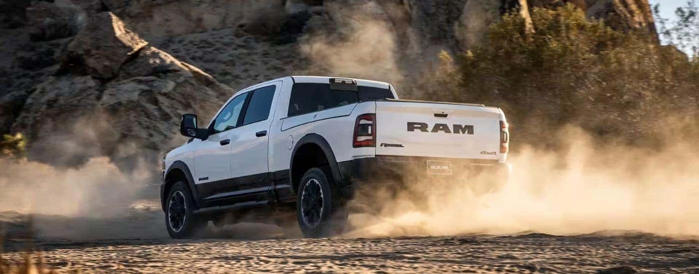 Rear view of a white 2024 Ram 2500 Rebel kicking up dust while off-roading.