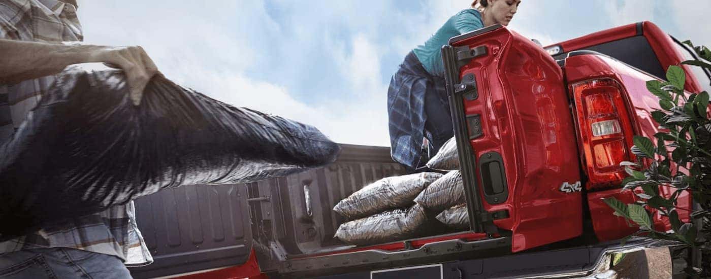 People loading mulch into the bed of a red 2025 Ram 1500 Big Horn