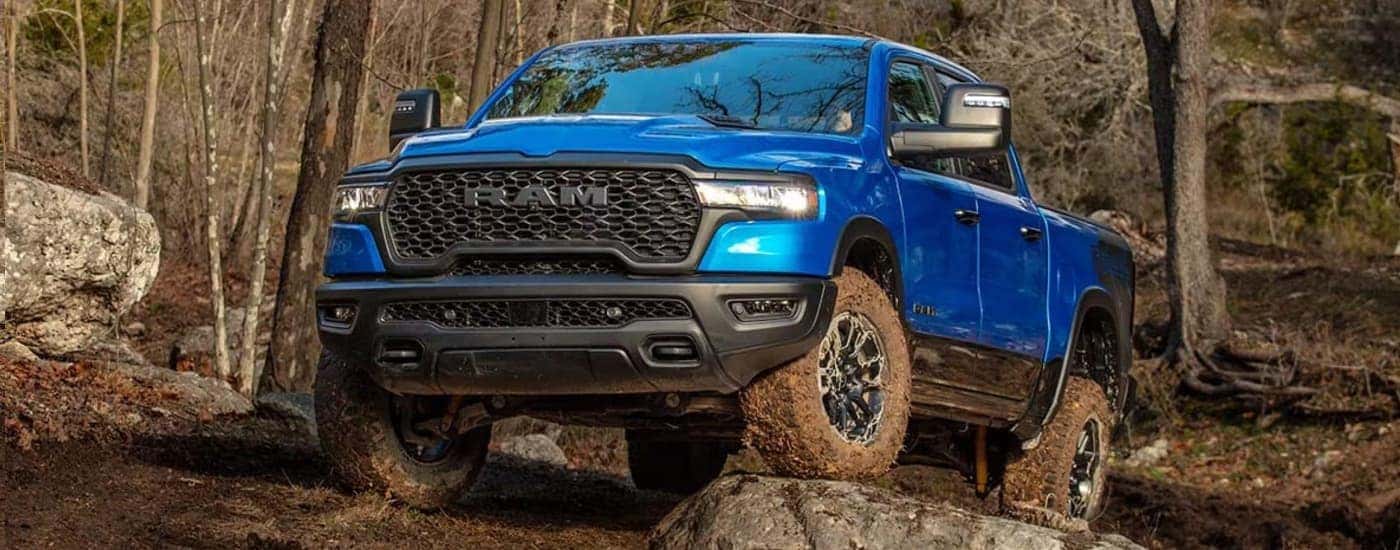 A blue 2025 Ram 1500 Rebel is off-roading on muddy trail.
