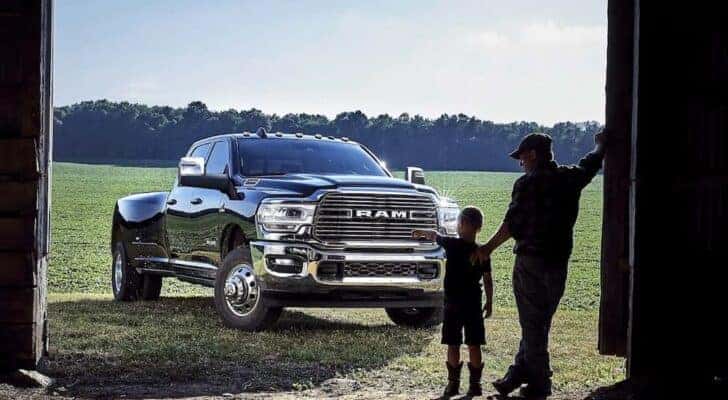 A black 2024 Ram 3500 HD is parked outside of a farm door in a grassy field.
