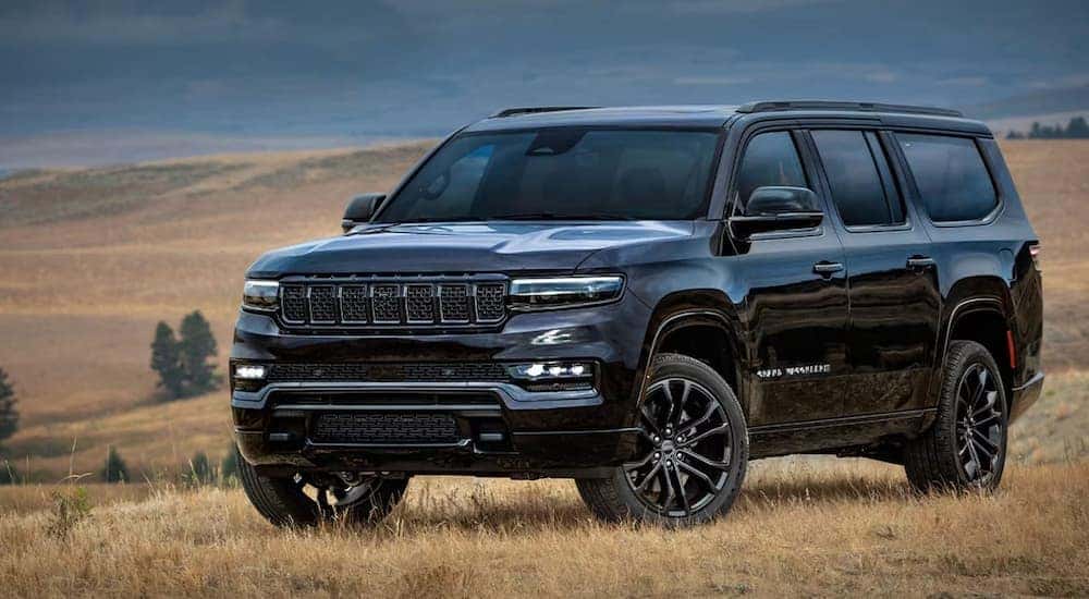 Right angled view of a black 2025 Jeep Grand Wagoneer for sale parked in a field.