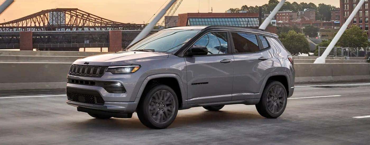 A gray Used 2022 Jeep Compass for sale driving on a bridge.