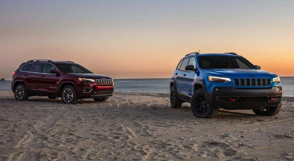 A red 2020 Jeep Cherokee and blue Cherokee Trailhawk parked on a coast.