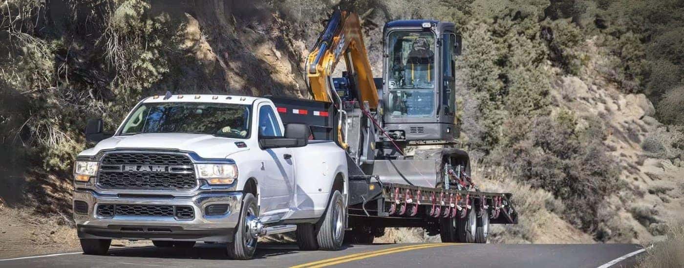 A popular used Ram for sale, a white 2024 Ram 3500, is towing construction equipment.