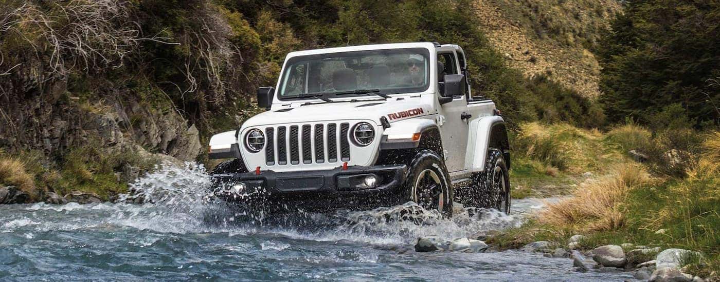 A white 2023 Jeep Wrangler Rubicon driving through a shallow river.