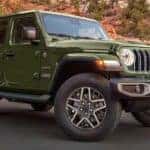 A green 2024 Jeep Wrangler Sahara is shown parked near a rocky hill.