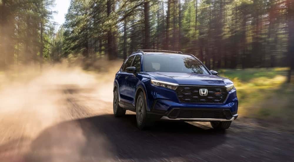 Blue 2026 Honda CR-V Hybrid TrailSport driving on a tree-line trail